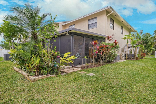 back of house featuring a sunroom, central AC unit, a lawn, and stucco siding