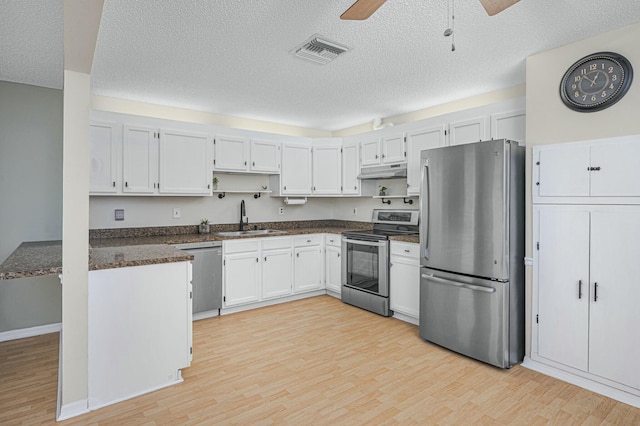 kitchen featuring under cabinet range hood, stainless steel appliances, a sink, visible vents, and dark countertops