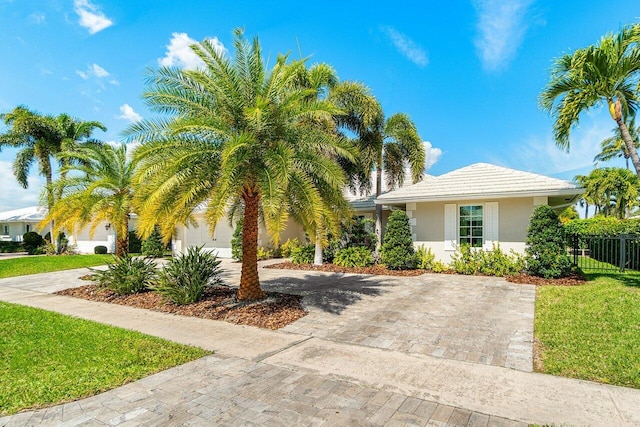 view of front of home featuring fence, a front yard, stucco siding, decorative driveway, and a garage