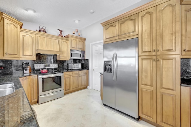 kitchen with a sink, decorative backsplash, dark stone counters, and stainless steel appliances