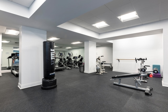 gym featuring a paneled ceiling and baseboards