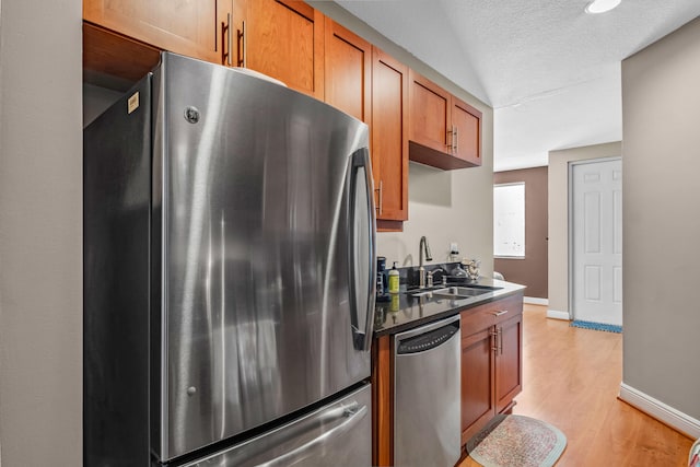 kitchen featuring stainless steel appliances, dark countertops, light wood-style floors, a sink, and baseboards