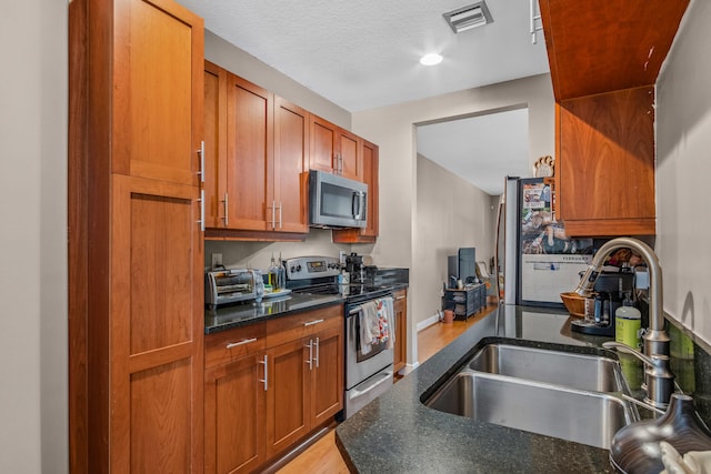 kitchen with a toaster, visible vents, brown cabinetry, appliances with stainless steel finishes, and a sink