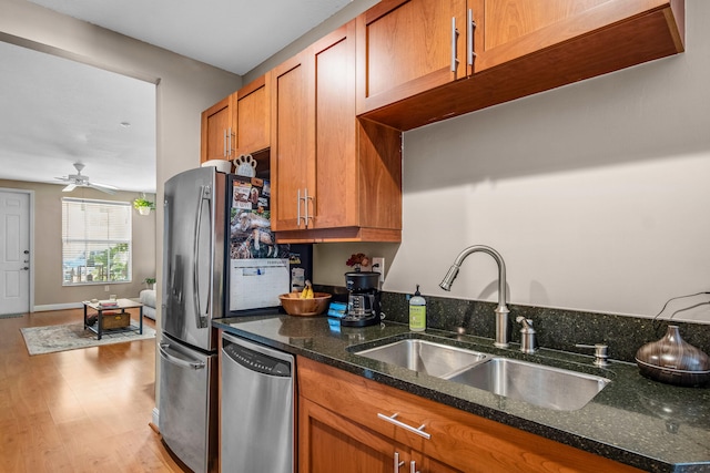 kitchen featuring stainless steel dishwasher, brown cabinetry, dark stone counters, a sink, and light wood-type flooring