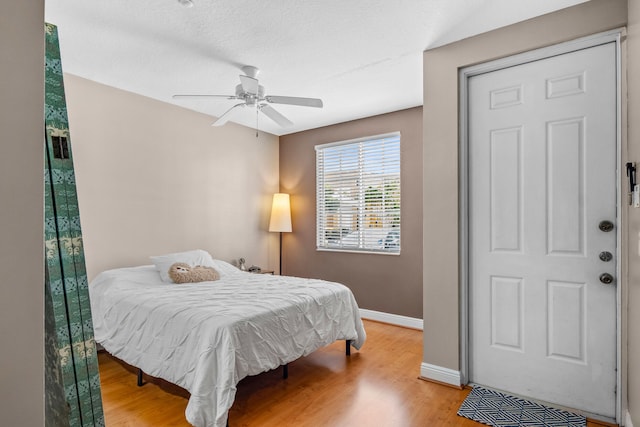 bedroom featuring a ceiling fan, a textured ceiling, baseboards, and wood finished floors