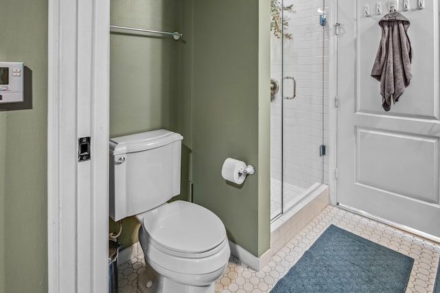 bathroom with toilet, a stall shower, and baseboards