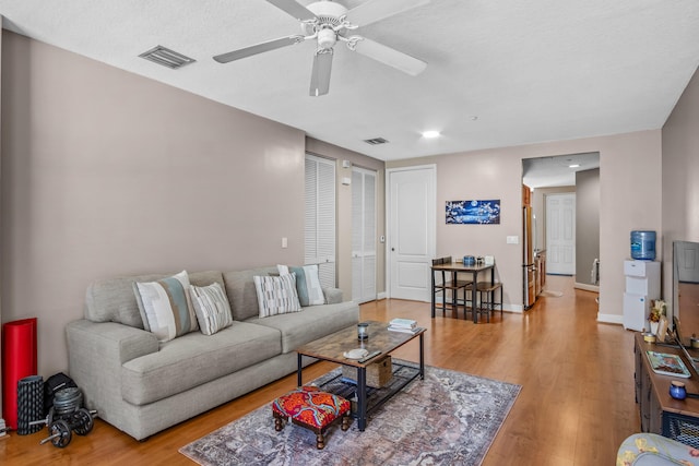 living area featuring ceiling fan, wood finished floors, visible vents, and baseboards