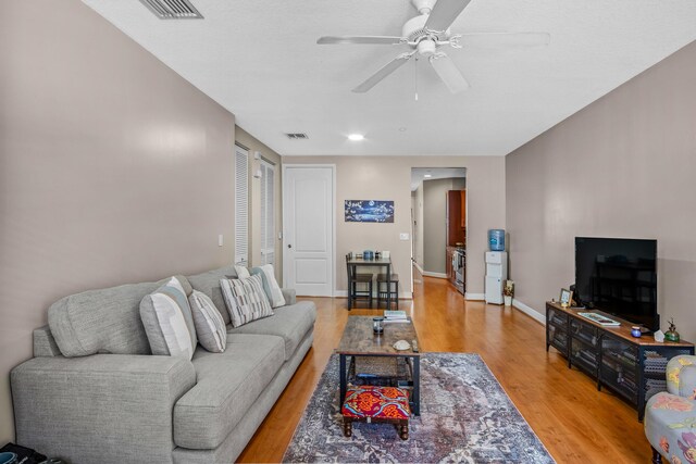 living room featuring a ceiling fan, visible vents, baseboards, and wood finished floors