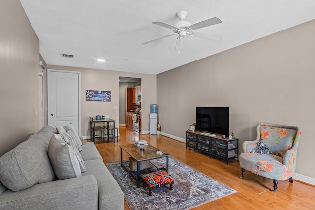 living room featuring ceiling fan, visible vents, baseboards, and wood finished floors