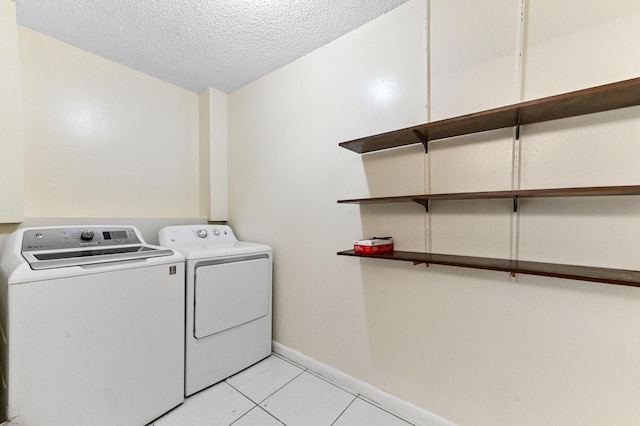 clothes washing area featuring a textured ceiling, washing machine and dryer, light tile patterned flooring, baseboards, and laundry area