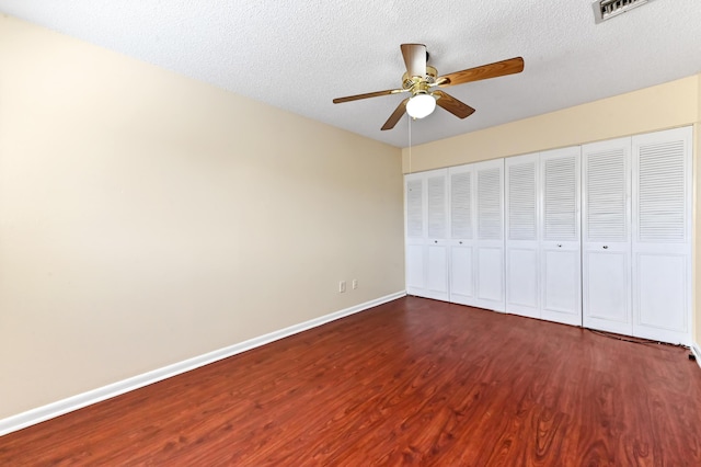 unfurnished bedroom featuring visible vents, a textured ceiling, baseboards, and dark wood-style flooring