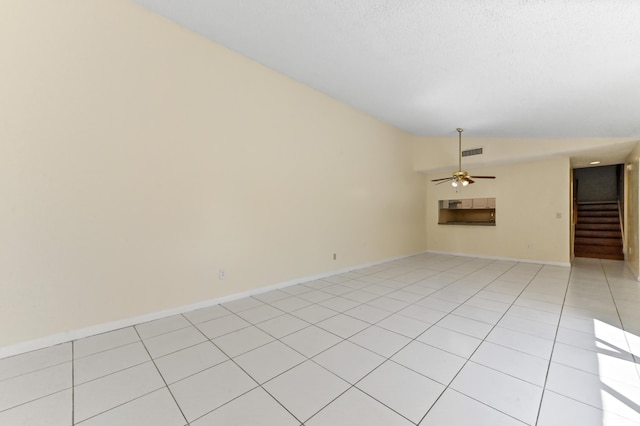 unfurnished room featuring light tile patterned floors, baseboards, ceiling fan, stairs, and vaulted ceiling