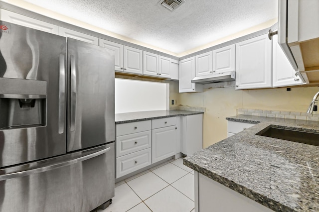 kitchen featuring light tile patterned floors, visible vents, dark stone counters, stainless steel fridge with ice dispenser, and a sink