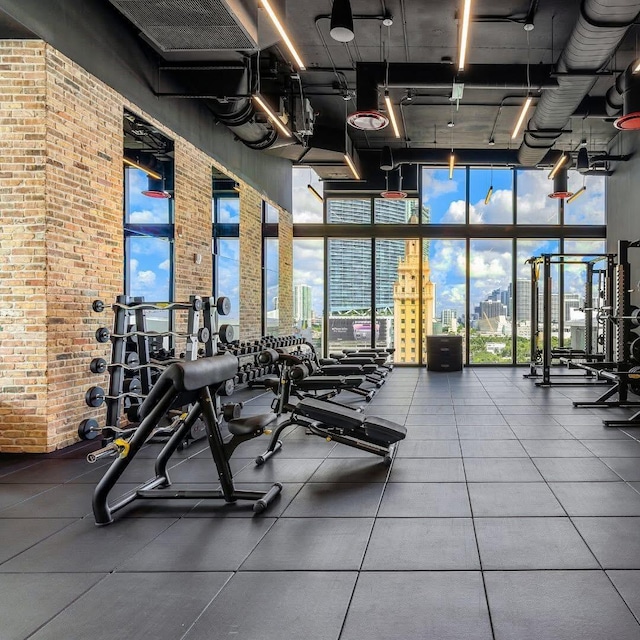 workout area with expansive windows, brick wall, and a view of city