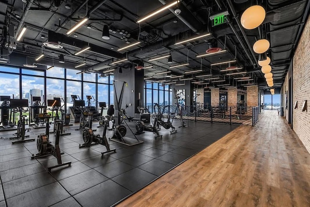 gym with a view of city, floor to ceiling windows, brick wall, and wood finished floors