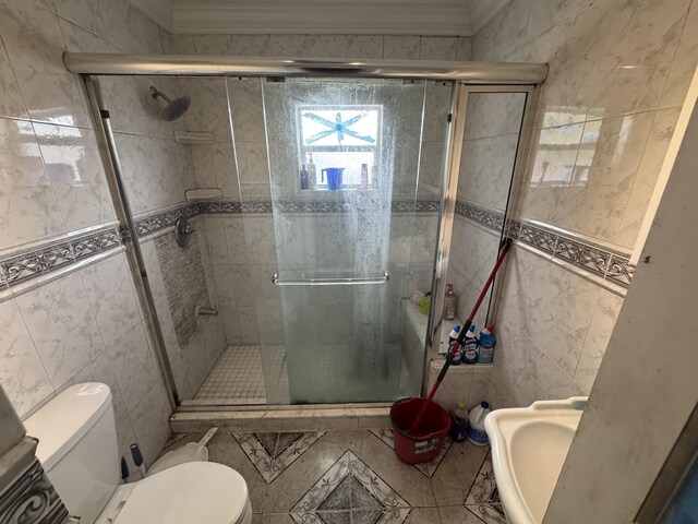 bathroom with toilet, a shower stall, a sink, and tile walls