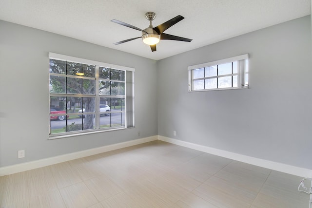 empty room with a textured ceiling, a ceiling fan, and baseboards