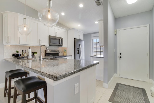 kitchen featuring visible vents, decorative backsplash, appliances with stainless steel finishes, a peninsula, and stone counters