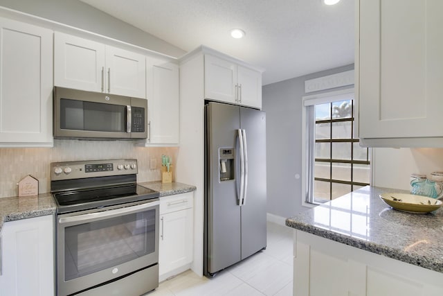 kitchen with appliances with stainless steel finishes, white cabinetry, decorative backsplash, and light stone countertops