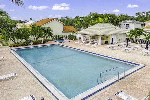 community pool with a patio area, fence, and a hot tub