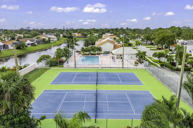 view of tennis court featuring a residential view, a water view, and fence