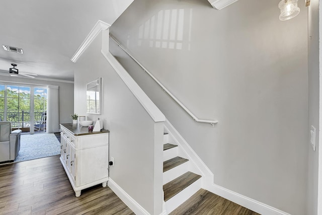 stairway featuring ceiling fan, wood finished floors, visible vents, baseboards, and crown molding