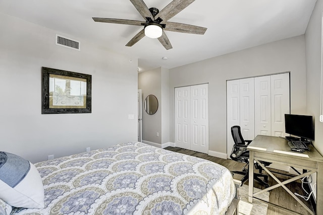 bedroom with two closets, visible vents, a ceiling fan, wood finished floors, and baseboards