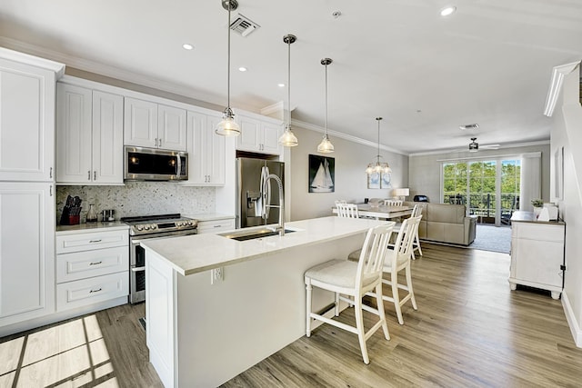 kitchen with crown molding, backsplash, appliances with stainless steel finishes, light wood-style floors, and a sink