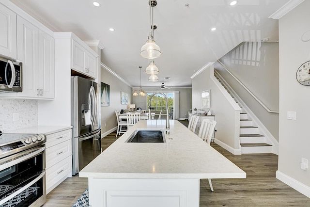 kitchen with crown molding, light wood finished floors, appliances with stainless steel finishes, white cabinetry, and an island with sink