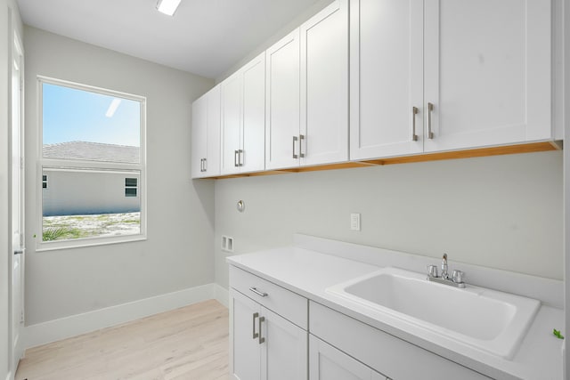 clothes washing area with cabinet space, baseboards, light wood-type flooring, washer hookup, and a sink