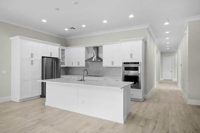 kitchen featuring crown molding, light countertops, appliances with stainless steel finishes, a kitchen island with sink, and wall chimney range hood