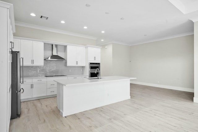 kitchen with stainless steel appliances, a sink, wall chimney exhaust hood, tasteful backsplash, and an island with sink