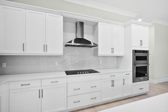 kitchen featuring white cabinetry, light countertops, wall chimney exhaust hood, and black electric cooktop