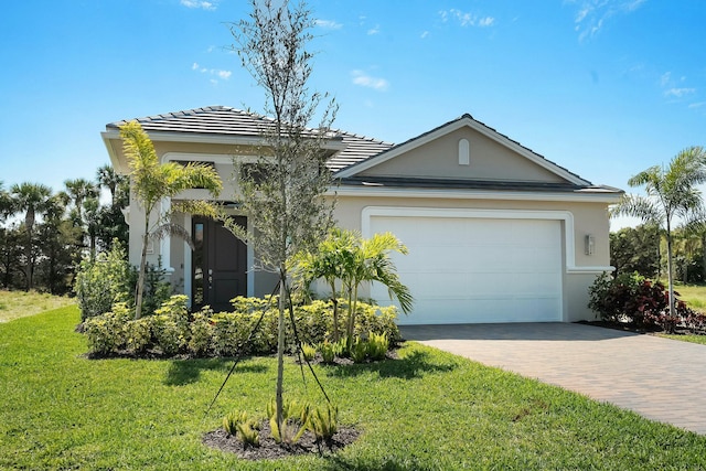 view of front of property featuring a tile roof, an attached garage, decorative driveway, a front lawn, and stucco siding