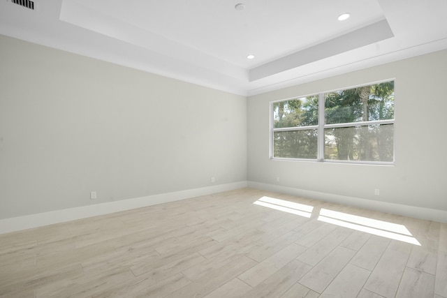 spare room featuring light wood finished floors, a tray ceiling, recessed lighting, and baseboards