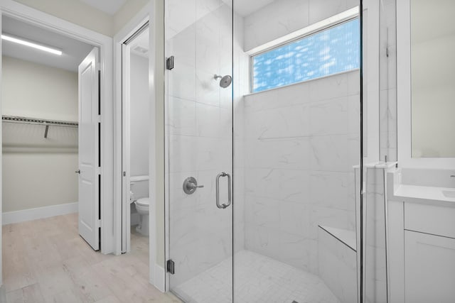 full bath with a spacious closet, toilet, a shower stall, wood finished floors, and baseboards