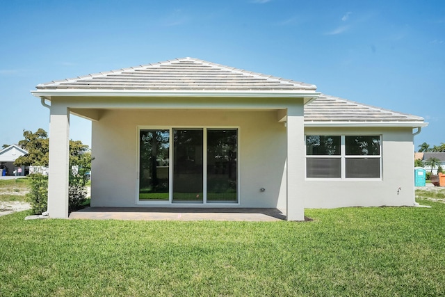 rear view of house featuring a lawn, a patio area, a tile roof, and stucco siding