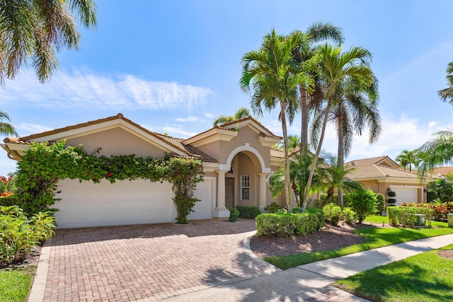 mediterranean / spanish house with a garage, a tiled roof, decorative driveway, and stucco siding