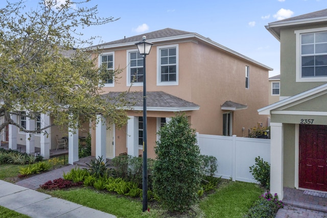 traditional-style home with a shingled roof, fence, and stucco siding