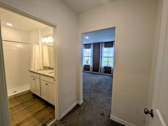 full bathroom with baseboards, wood finished floors, tiled shower, and vanity