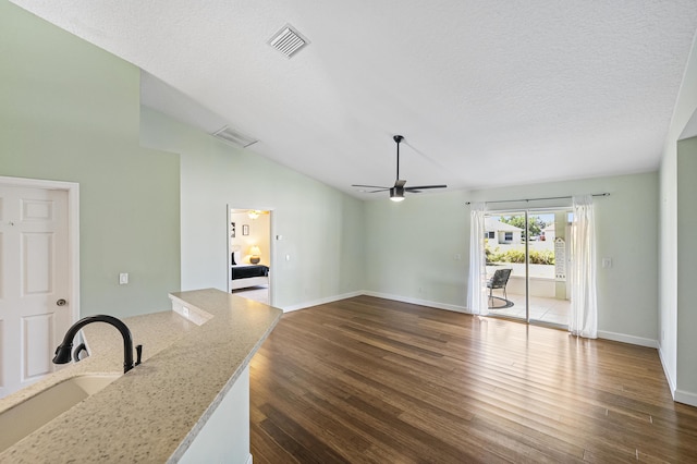 unfurnished living room with visible vents, dark wood-style flooring, a sink, vaulted ceiling, and a textured ceiling