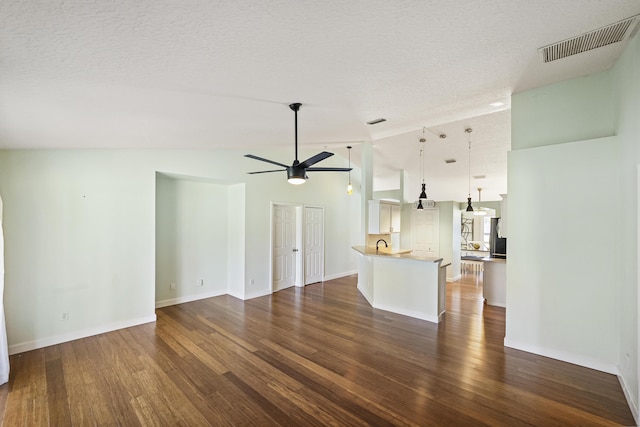 unfurnished living room featuring a textured ceiling, dark wood-style floors, visible vents, and ceiling fan