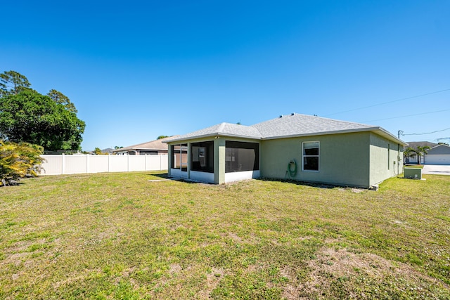 rear view of house featuring stucco siding, a sunroom, a lawn, and fence