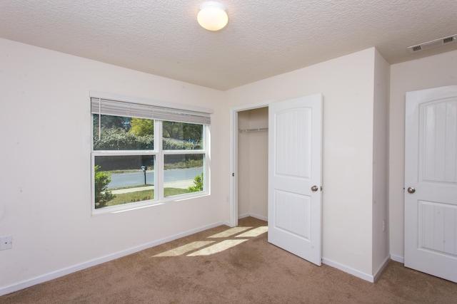 unfurnished bedroom with a closet, a textured ceiling, visible vents, carpet, and baseboards