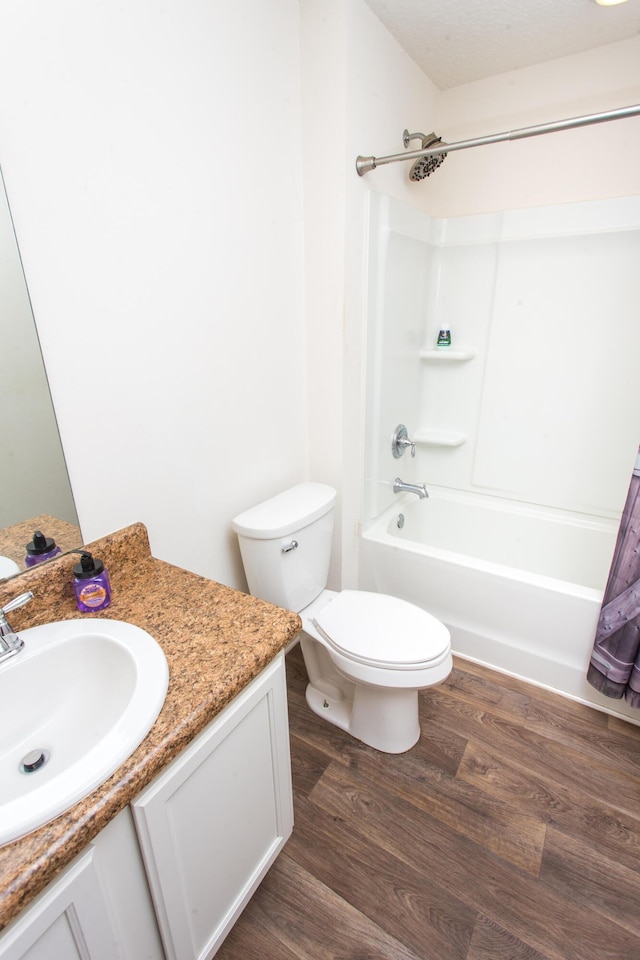 full bath with washtub / shower combination, toilet, wood finished floors, and vanity
