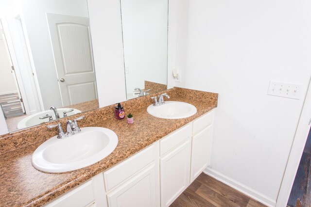 full bath with double vanity, a sink, and wood finished floors