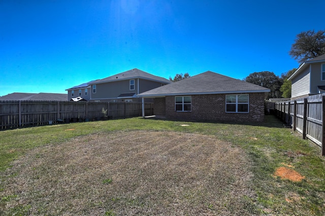 back of house with a fenced backyard, brick siding, and a yard