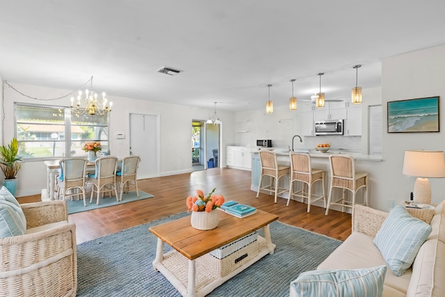 living room with ceiling fan with notable chandelier, wood finished floors, visible vents, and baseboards