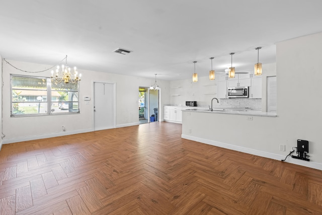 unfurnished living room with visible vents, ceiling fan with notable chandelier, baseboards, and a sink