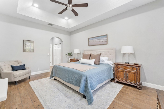 bedroom featuring light wood-type flooring, visible vents, arched walkways, and a raised ceiling